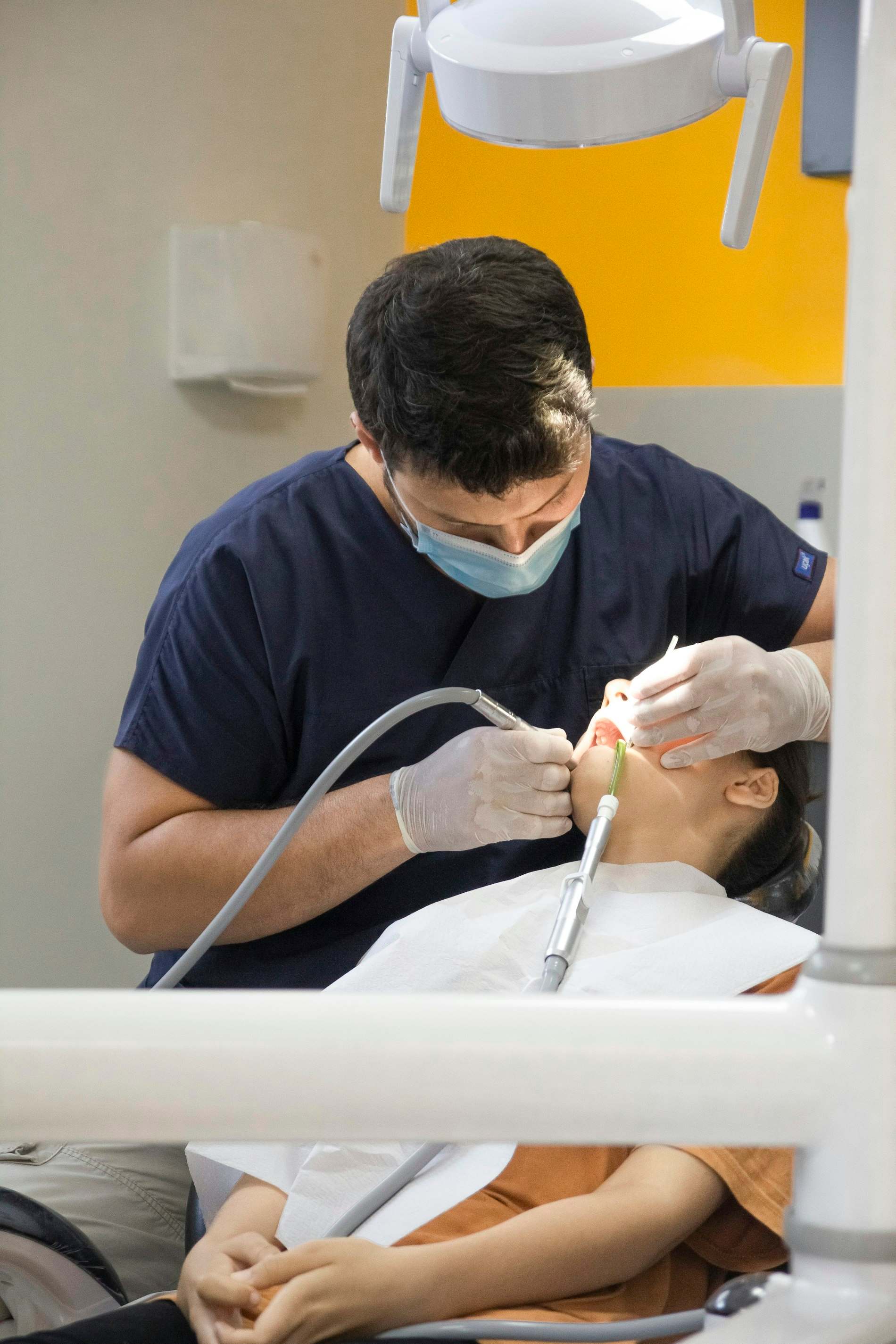 Dentista de máscara e luvas atendendo um paciente na cadeira