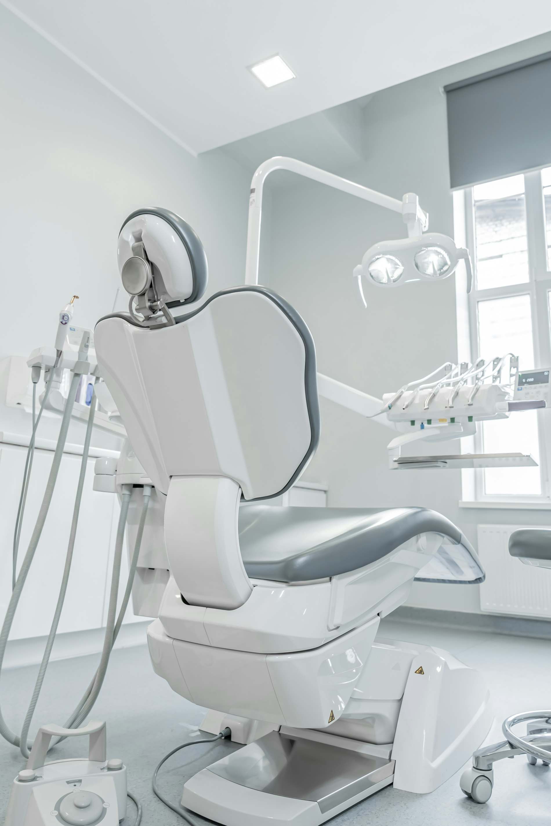 Cadeira odontológica branca ao lado de uma janela com luz natural