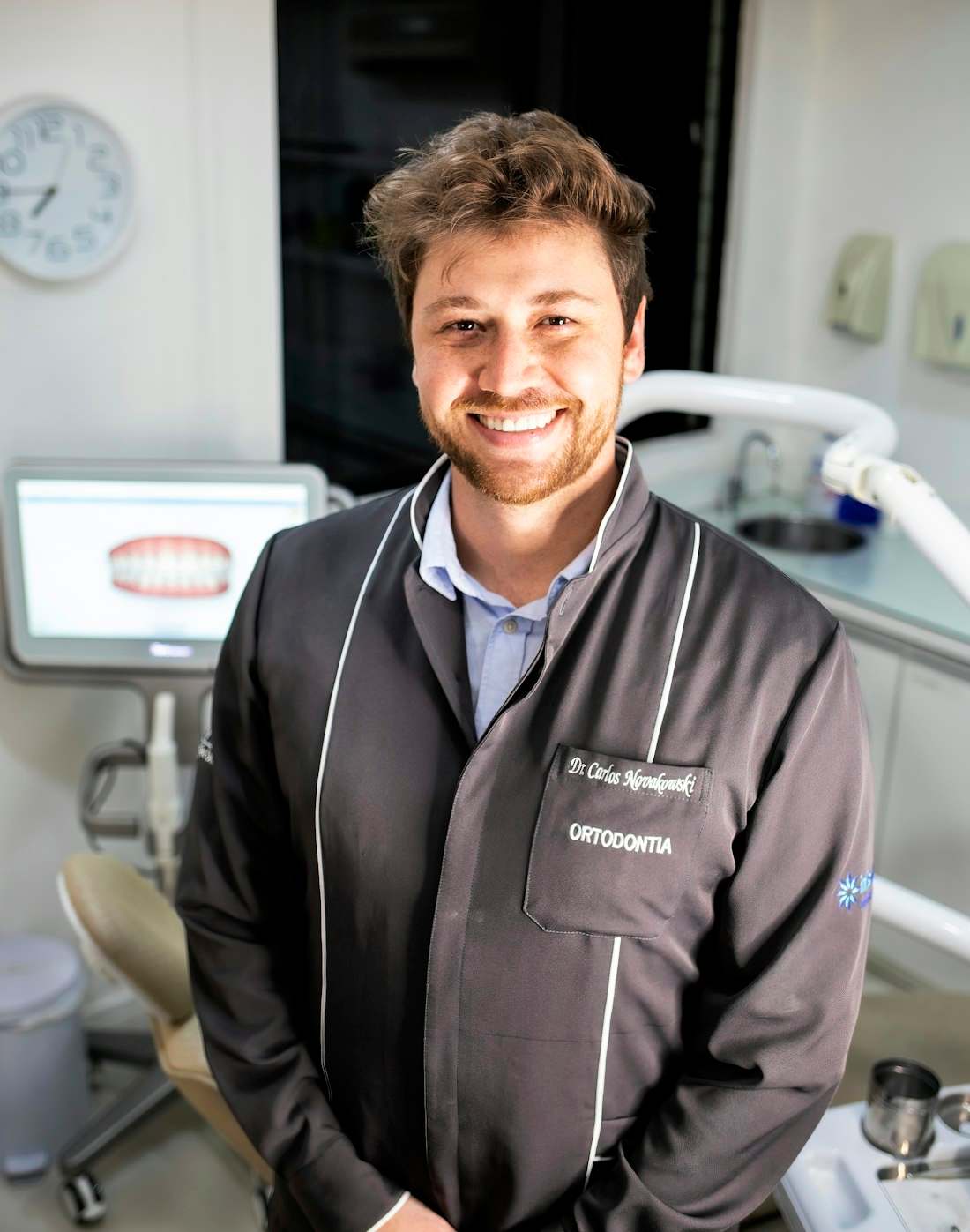 Dr. Henrique Cavalcanti Rocha, homem de barba e jaleco escuro, sorrindo no consultório