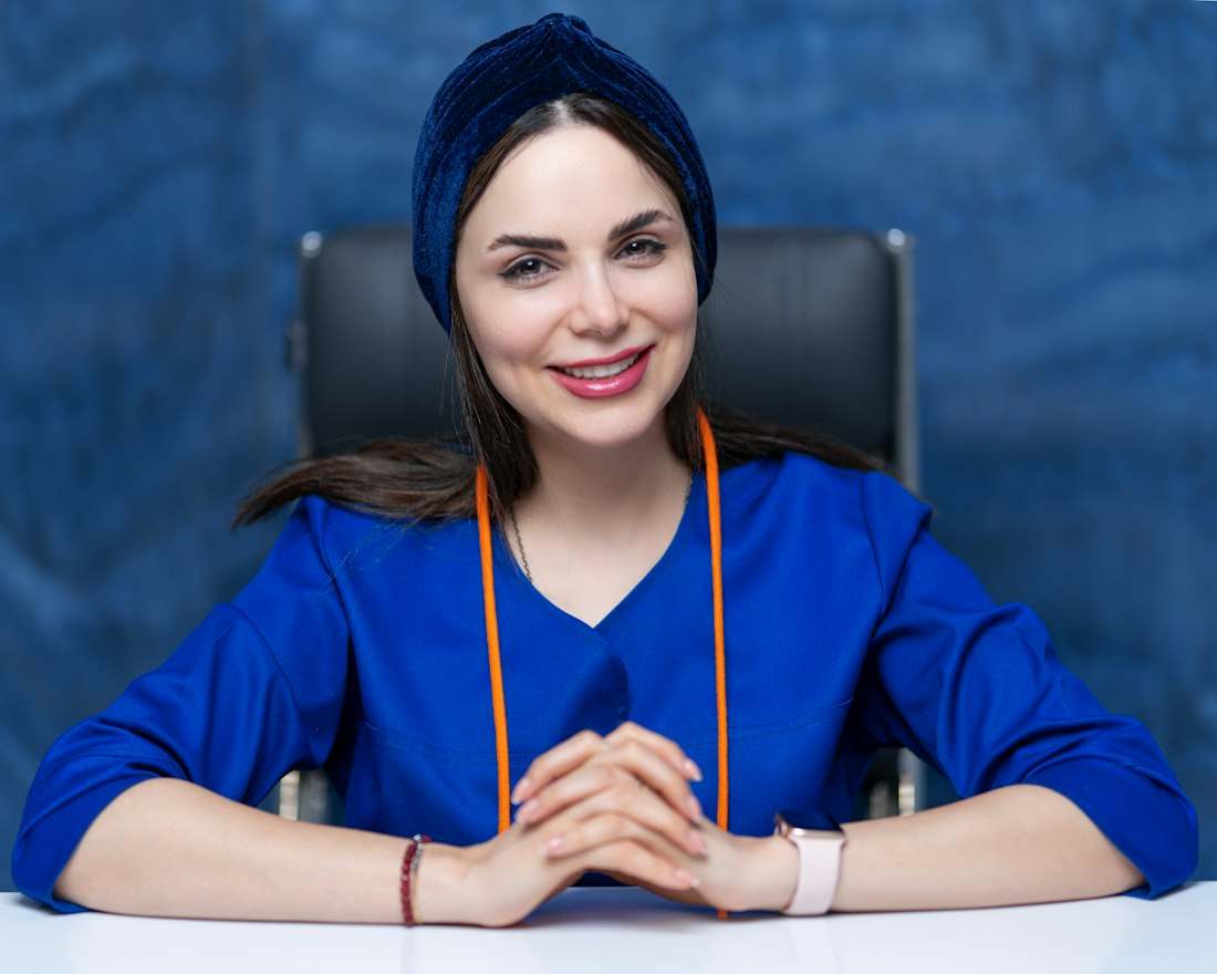Dra. Beatriz Farias Dantas, mulher de cabelo escuro e uniforme azul, sentada à mesa