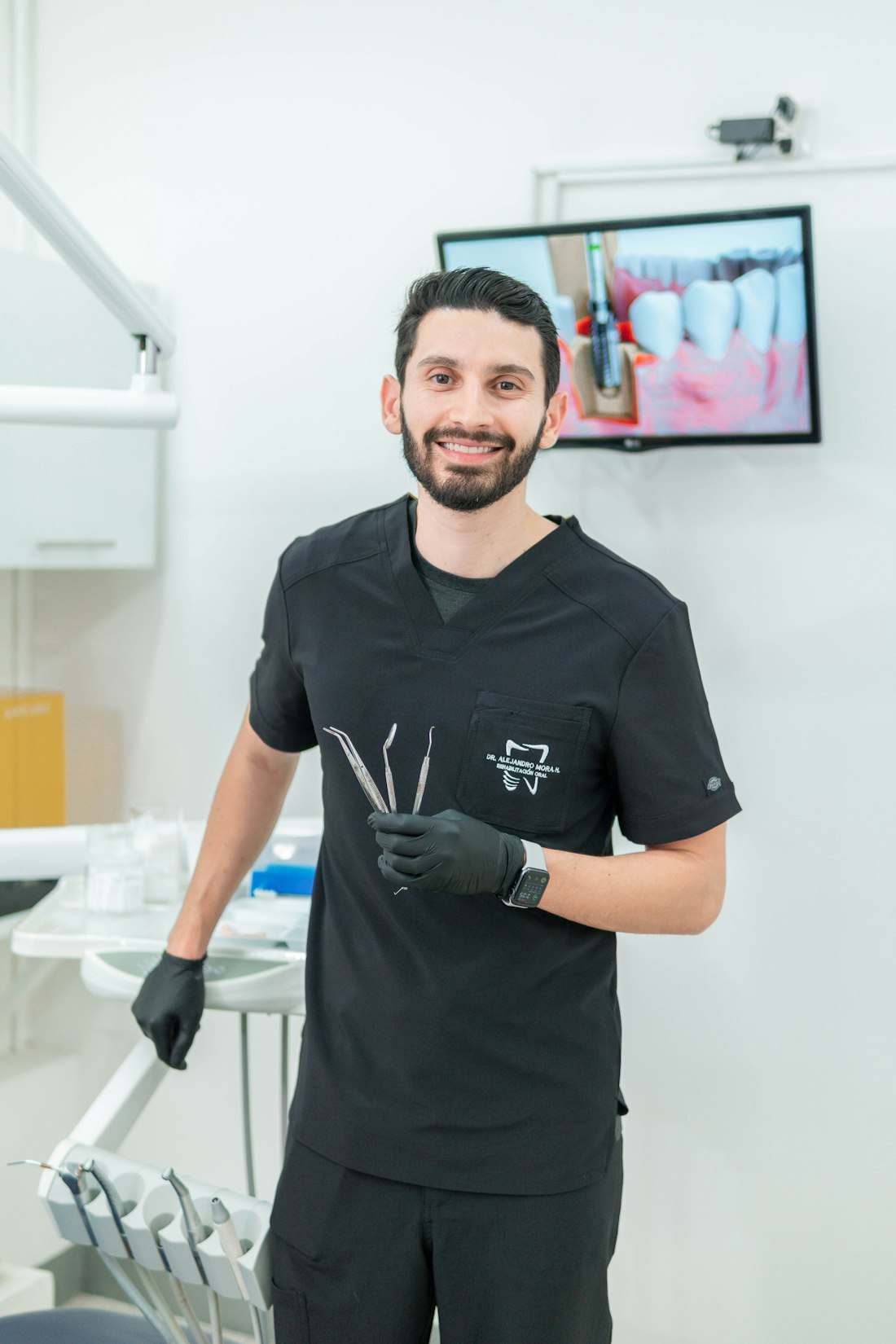 Dr. Rafael Moura Bezerra, homem de uniforme preto segurando instrumentos odontológicos