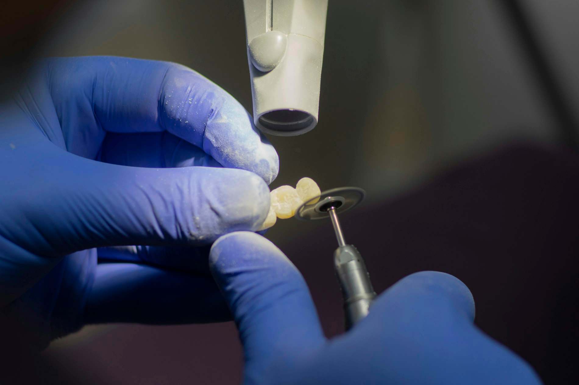 Mãos com luvas ajustando uma peça dental com instrumento fino